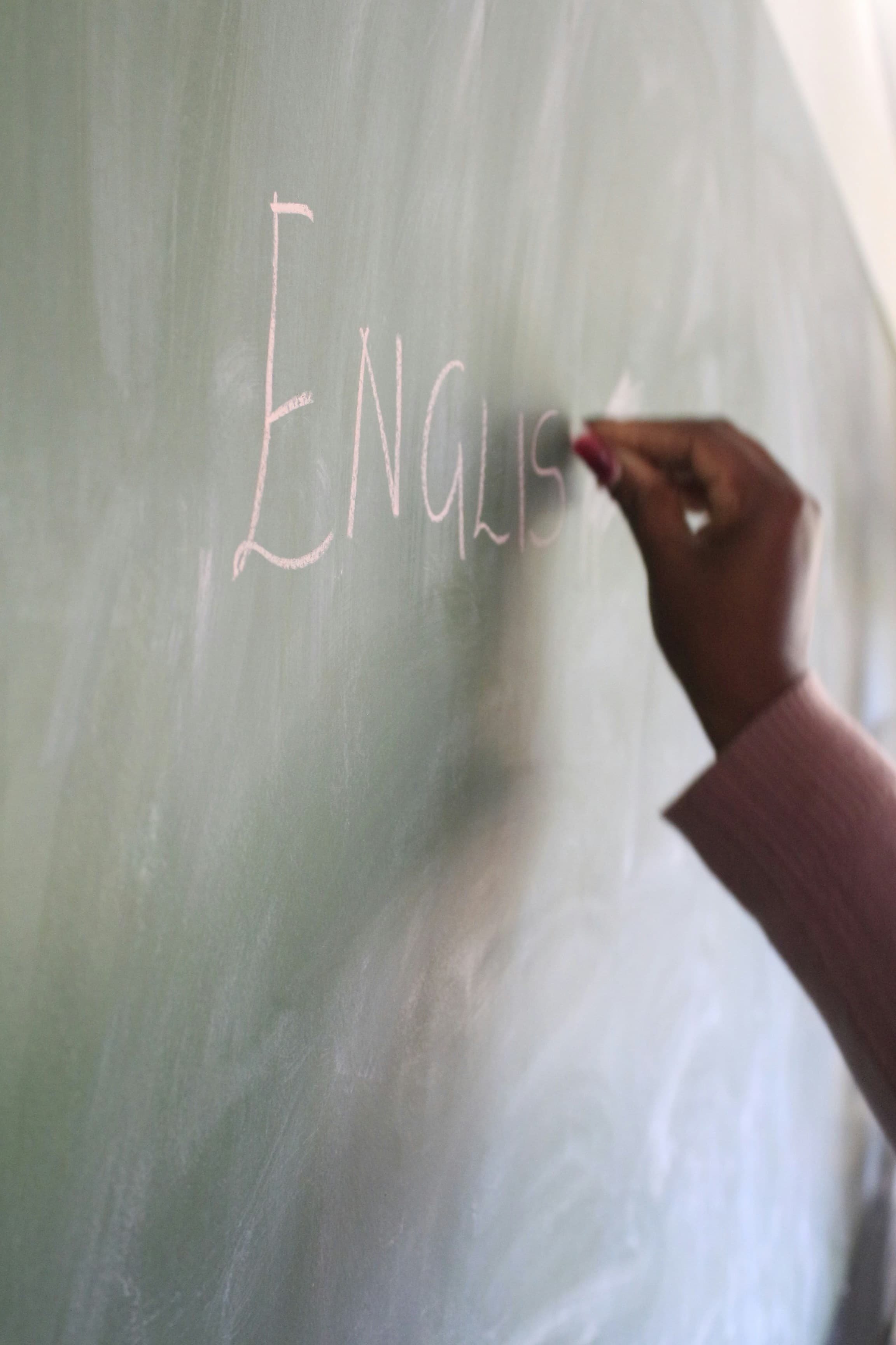 A hand writing on a green chalkboard